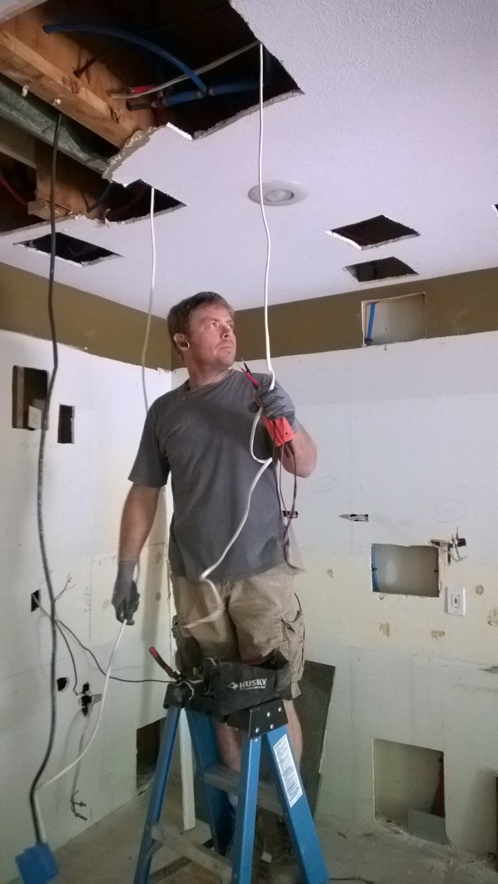 Chris on a ladder pulling new wire through an opened-up ceiling