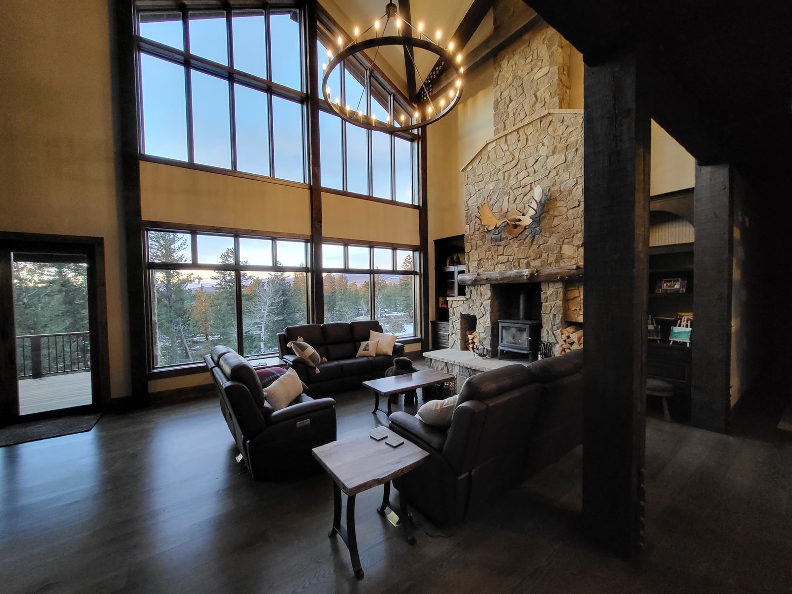The Cabin's great room at dusk: a wagon-wheel chandelier, tall windows, and a stone fireplace