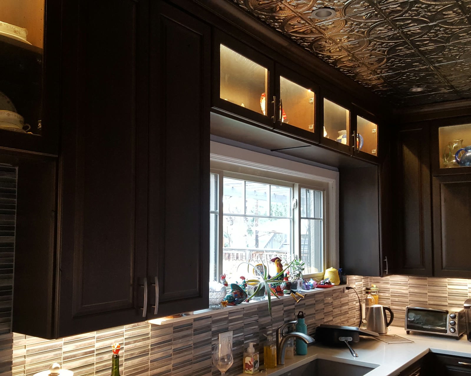 A kitchen with lit glass cabinets and under-cabinet lighting over a tile backsplash